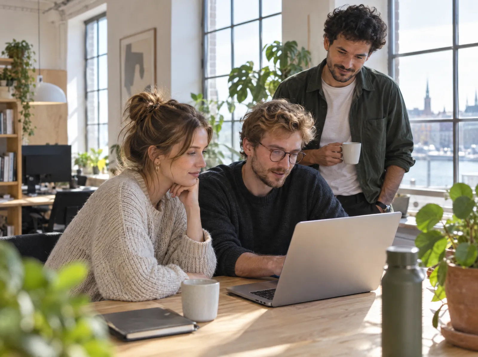 Three colleagues looking at a laptop together in a bright studio office
